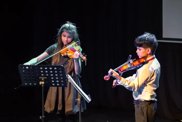 Two children playing violin on stage at a Tehran Pars concert