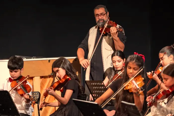 A violin teacher playing alongside his students on stage
